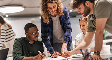 group of young professionals collaborating on a project discussing ideas and taking notes in a modern workspace focused on teamwork and creativity in 2022