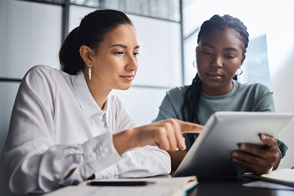 Two women engaged in a discussion while reviewing information on a tablet in a modern workspace showcasing collaboration and learning with 8 ideas for success