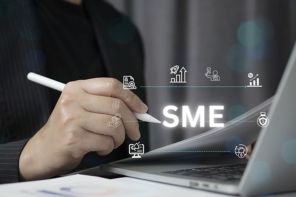 hand holding a pen writing SME on a notepad next to a laptop symbols representing growth and business strategies importance of SMEs and their role in the economy 9 strategies for success