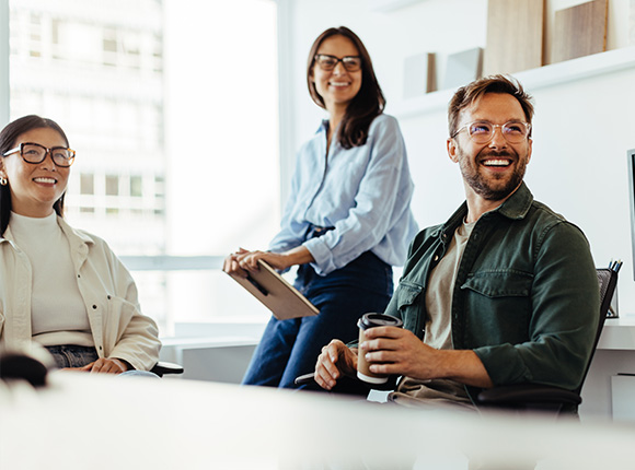 three smiling colleagues in a modern office setting engaging in conversation about innovative ideas for project eleven