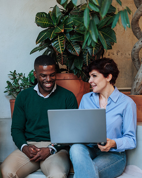 two individuals collaborating with a laptop in a casual setting surrounded by greenery