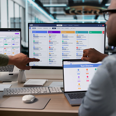 people collaborating at workspace with multiple computer displays showing a team directory and HR software interface working together to enhance seven team members management efficiency