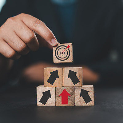 a hand placing a block with a target symbol on top of stacked blocks featuring arrows representing growth progress and success in achieving ten goals