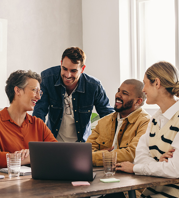 four professionals engaged in a collaborative discussion around a laptop in a modern workspace showcasing teamwork and creativity with six ideas being shared