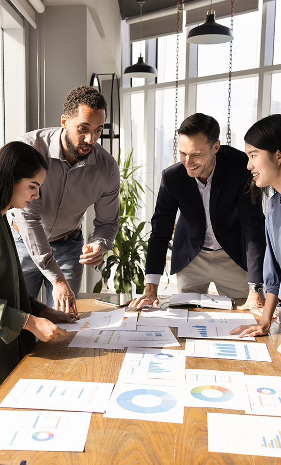 four professionals collaborating around a table analyzing six business charts and graphs in a modern office setting