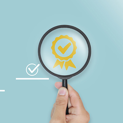 hand holding a magnifying glass over a yellow award ribbon with a check mark symbolizing quality assurance and verification of 9 key aspects