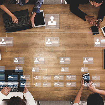 group of professionals collaborating at a table with laptops and devices displaying organizational charts depicting 11 roles