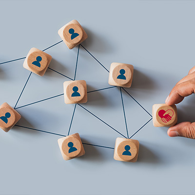 hand placing wooden block with heart icon among other blocks with people icons in a network of connections visualizing relationships and collaboration strategies in community building and teamwork